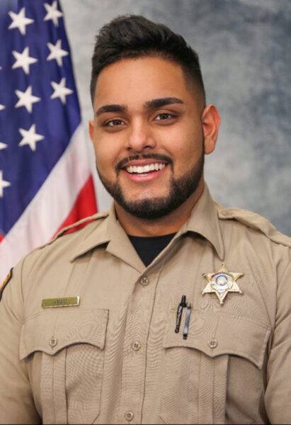 Hamza Khan in his deputy uniform, standing in front of an American flag