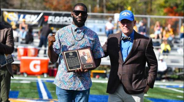 Jonas Randolph holds his Hall of Fame plaque while standing next to President Tony Floyd at midfield on the football field.