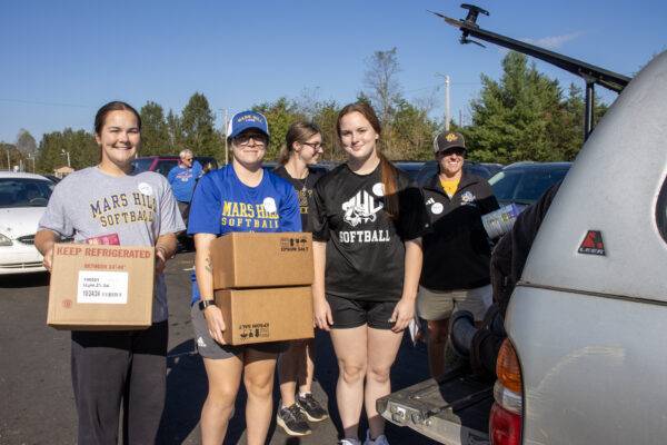 Students carry boxes of relief supplies and load them in the back of a vehicle.