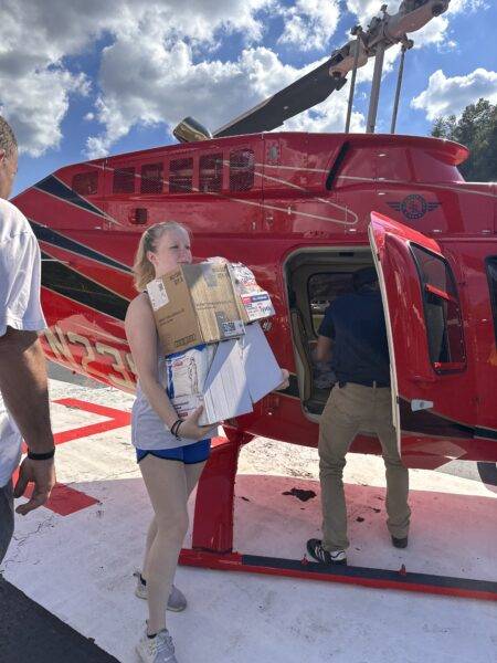 A student helps unload relief supplies from a red helicopter.