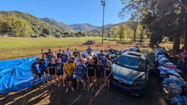 A large group of students and other volunteers poses for a photo in front of a field and mountain backdrop during a flooding clean-up service effort.