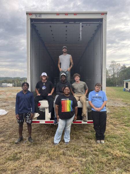 A group of students pauses for a break at the rear of a tractor-trailer of relief supplies.