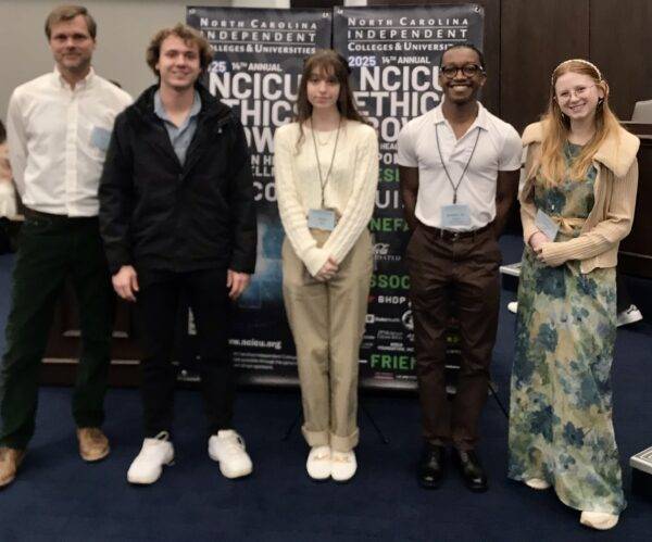 left to right: Ryan Bell, TJ Burske, Alexis Allen, AJ Rivers, and Cassie Berry pose in front of NCICU Ethics Bowl banners